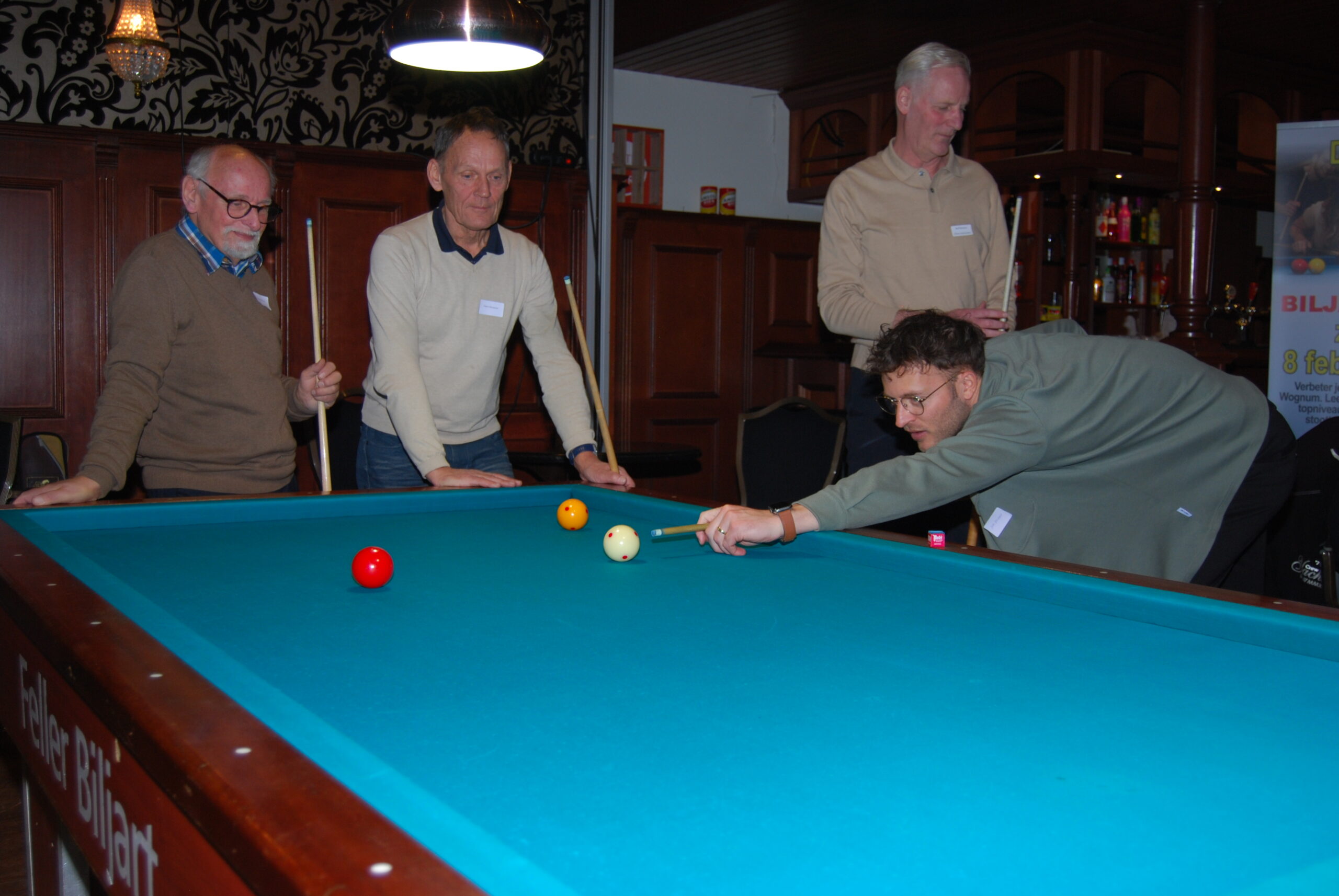 Deelnemers oefenen driebandenstoten tijdens de 4e Lions Biljartclinic in Opmeer onder begeleiding van leermeesters.