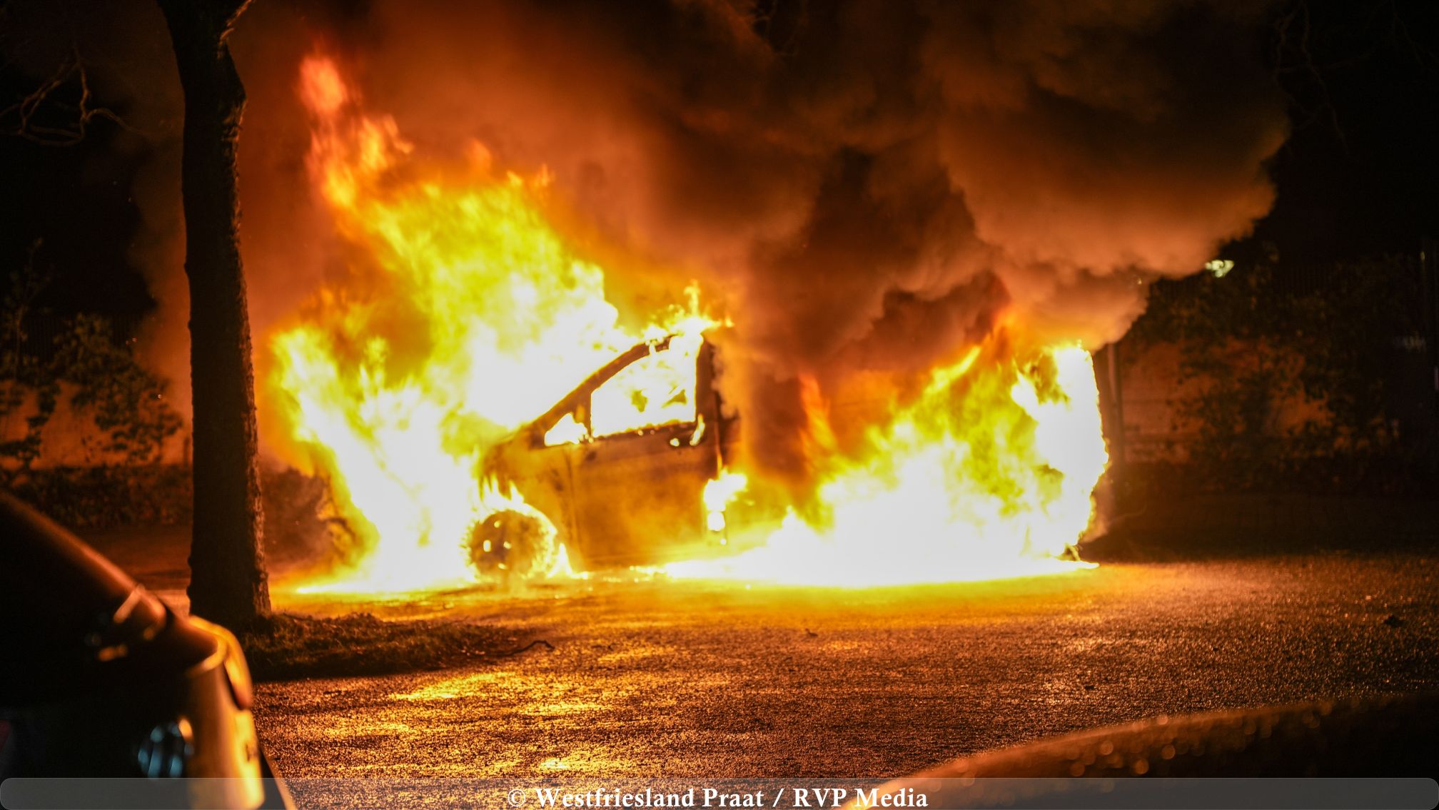 Brandweer blust een volledig uitgebrande bestelbus op een parkeerplaats in Hoorn tijdens de nacht.