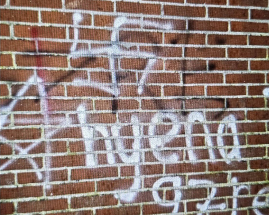 Racistische graffiti met hakenkruis op een muur, politie onderzoekt de bekladding.