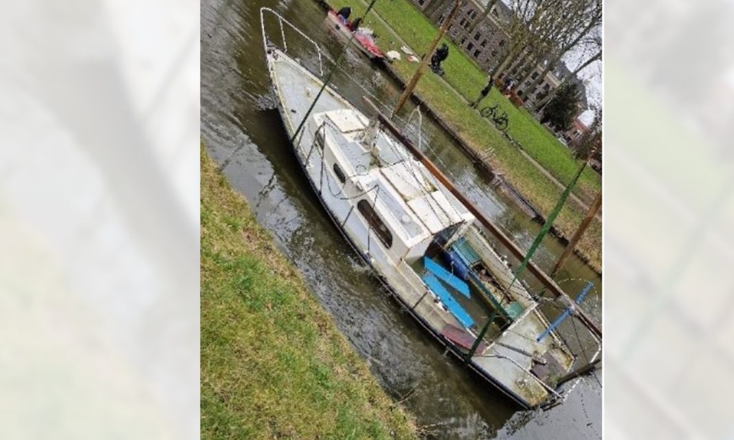 Verwaarloosde blauwe zeilboot in het water aan de Landswerf te Medemblik.